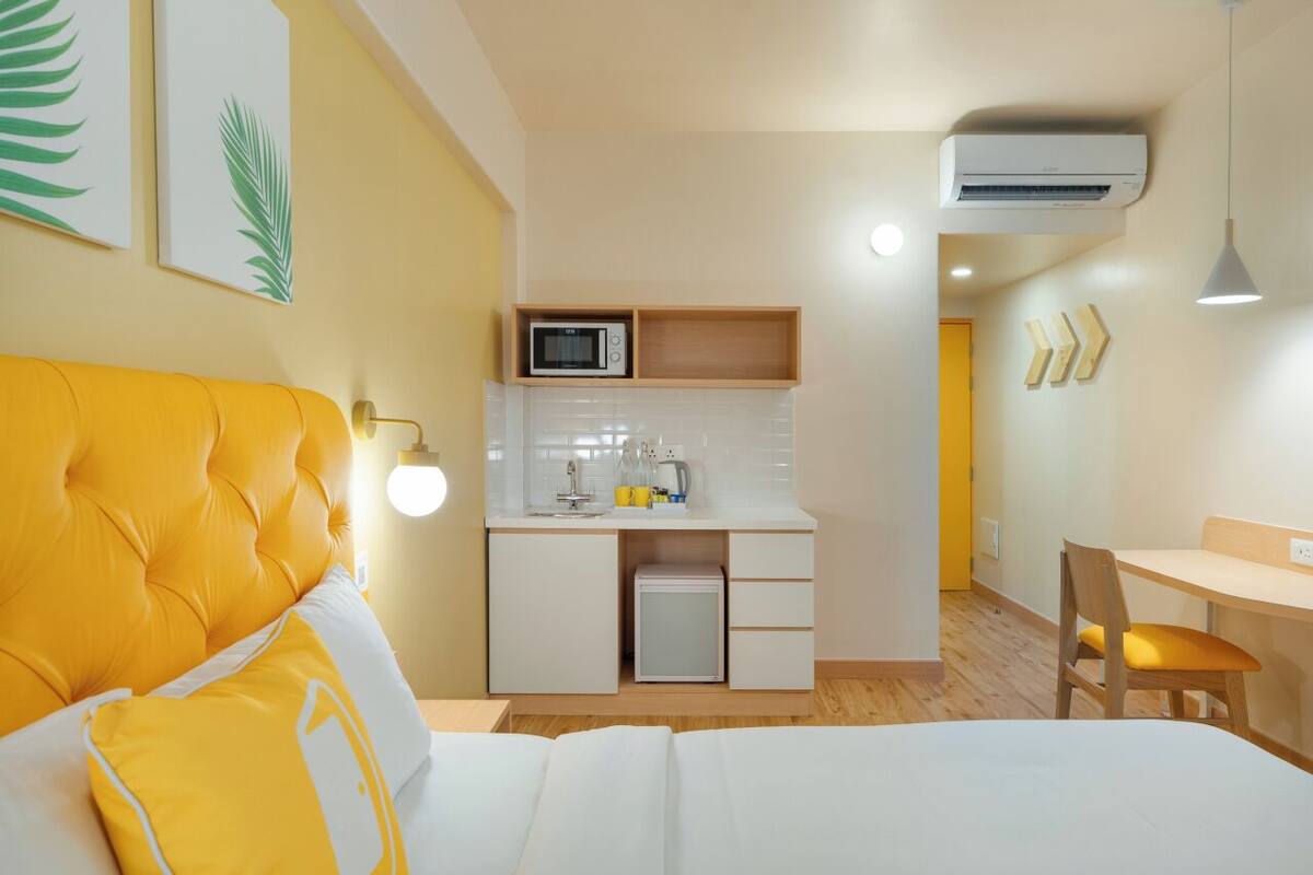 A compact hotel room with a bed, a small kitchenette, a dining area, and a bathroom.