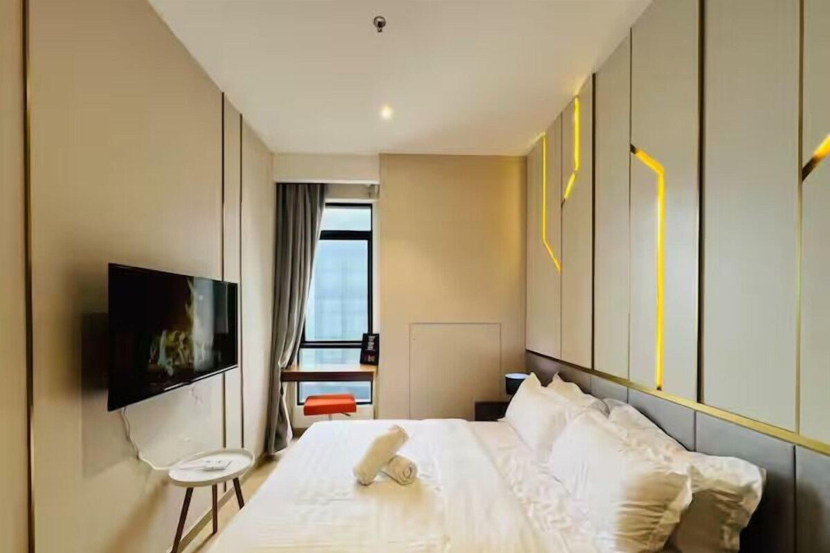 A modern hotel room with a bed, a TV, a small table, and a window with curtains.
