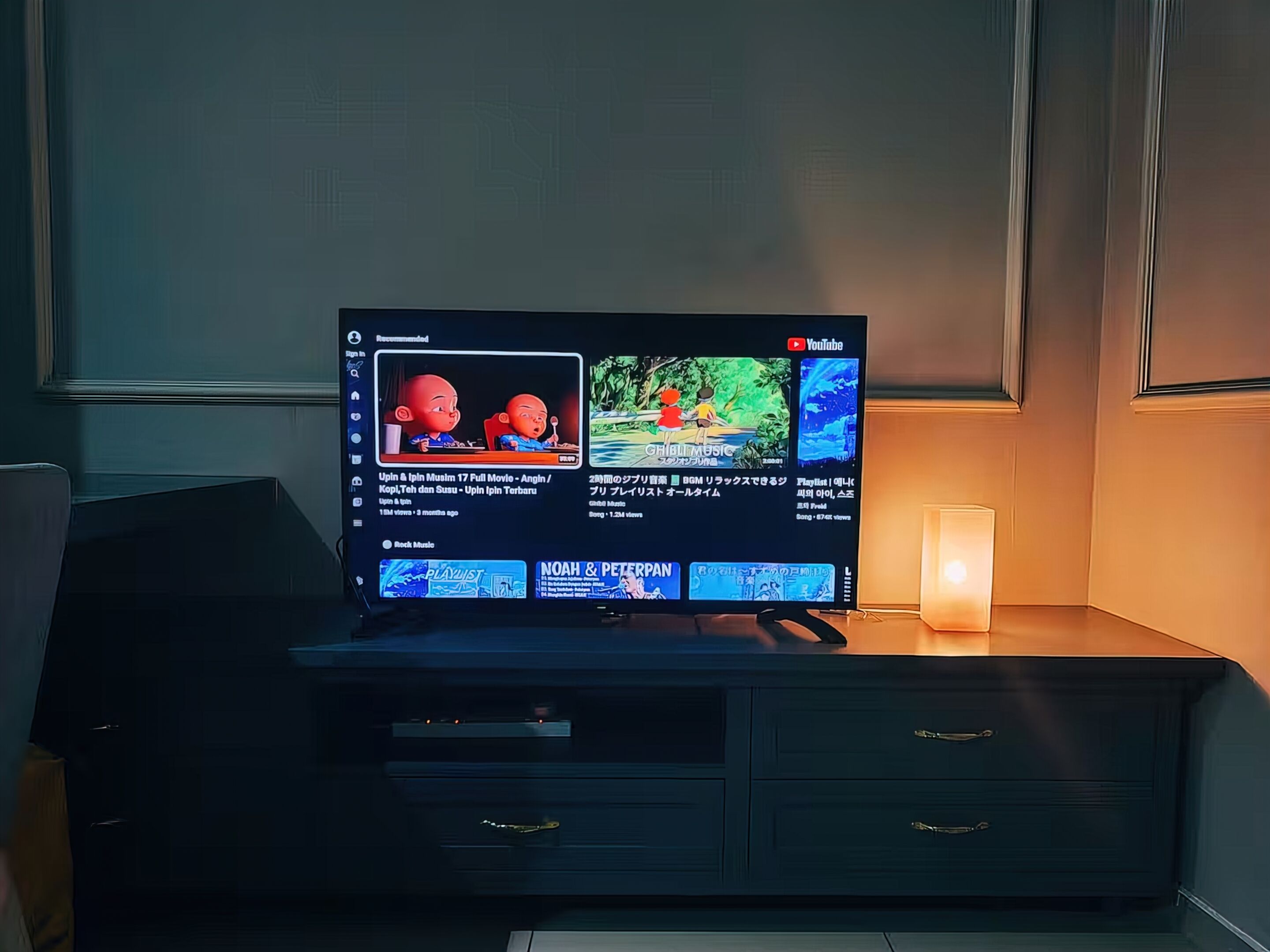 Un televisor sobre un mueble de madera oscura con una vela encendida a un lado.