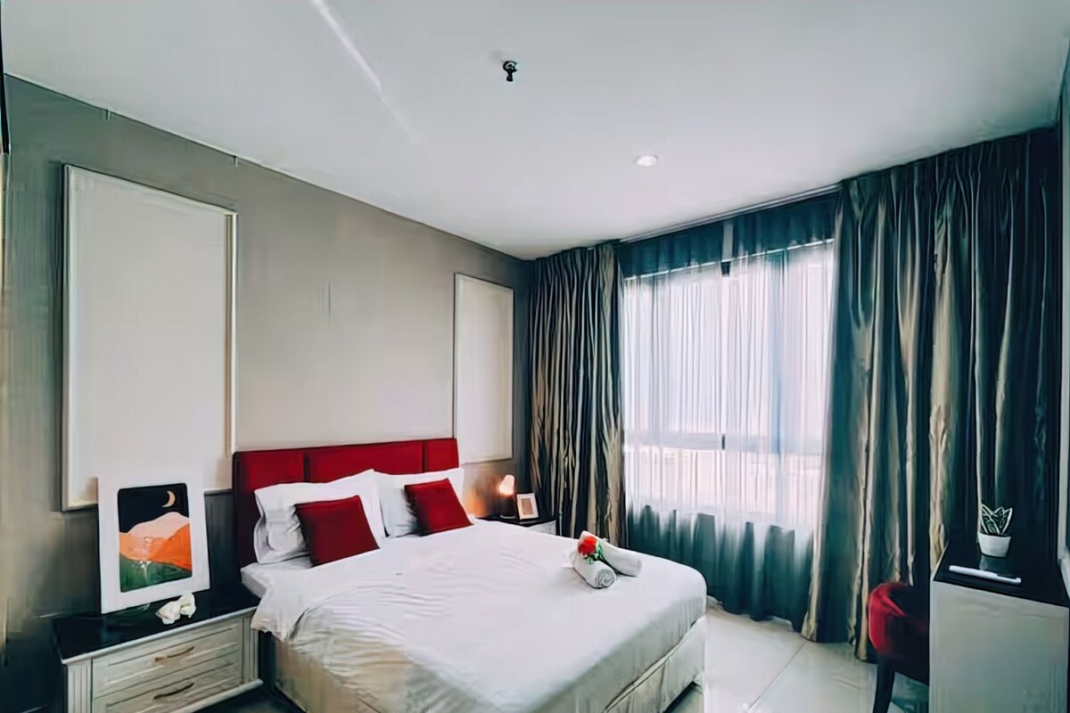 A modern hotel room with a large bed, a nightstand, a desk, and a window with curtains.