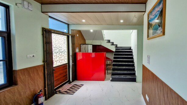 Un pasillo con una puerta de madera, un armario rojo, un extintor y una escalera que sube a otro nivel.