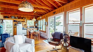 Een gezellig chaletinterieur met een eethoek, keuken en een groot raam met uitzicht op een waterpartij.