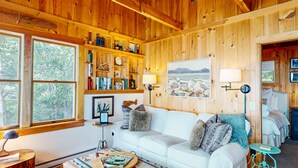Een gezellig chaletinterieur met een witte bank, houten planken en een groot raam.