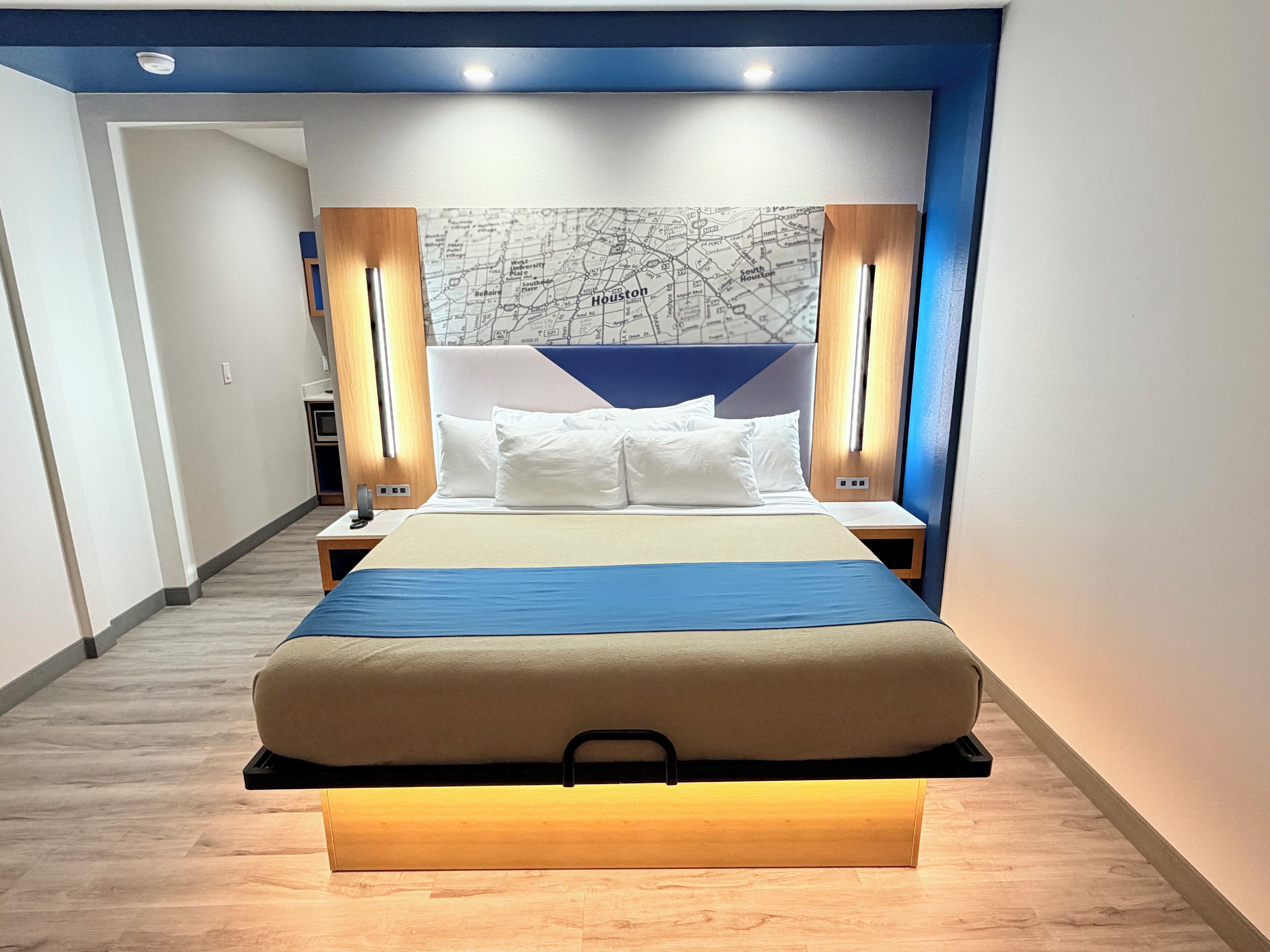 A modern hotel room with a large bed, a map on the wall, and a wooden nightstand.