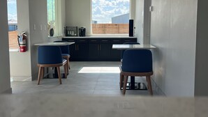 A modern kitchen with dark cabinets, a large window, and a dining area with blue chairs. - Crystal Inn - NorthWest - 290 (Houston)