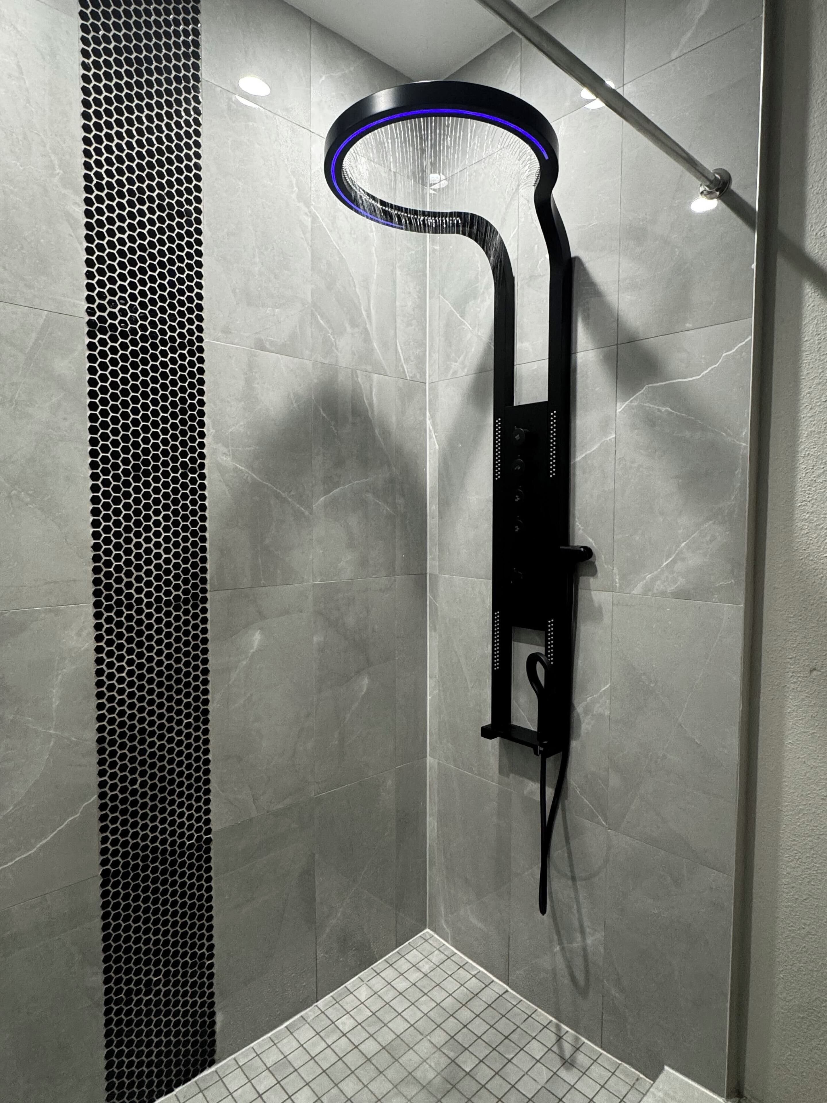 A modern shower with a curved design, a control panel, and a tiled floor.