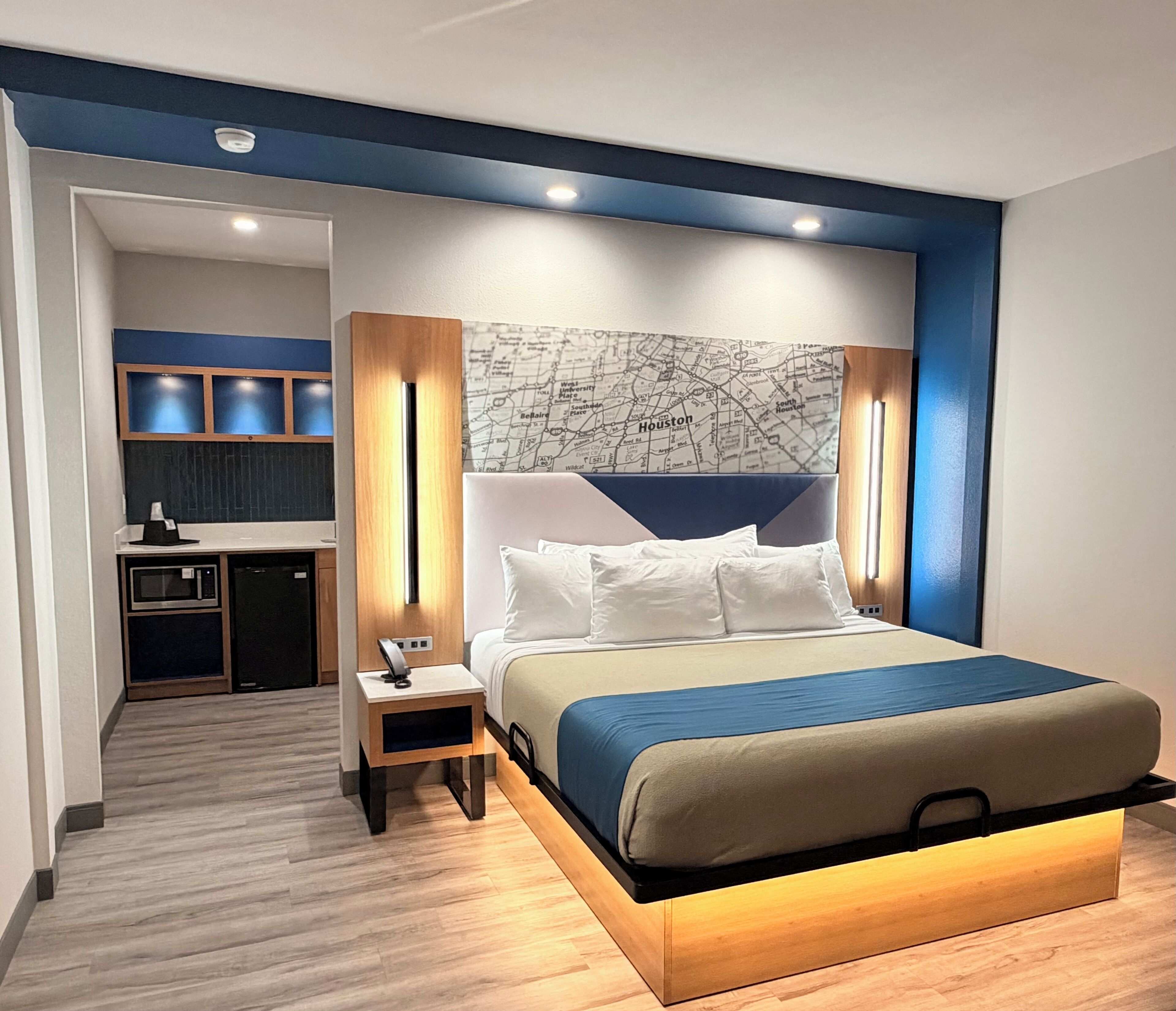 Una habitación de hotel moderna con una cama grande, un mapa en la pared y una kitchenette al fondo.