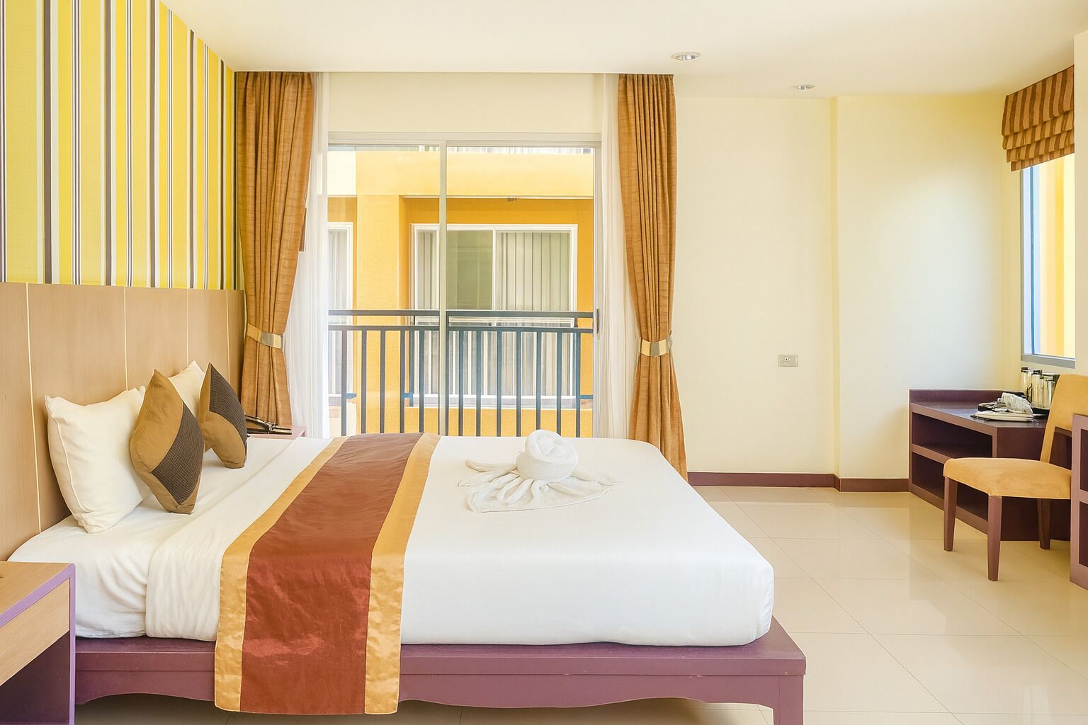 Habitación de hotel con cama, escritorio, silla y balcón con cortinas.