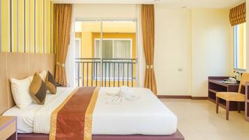 Habitación de hotel con cama, escritorio, silla y balcón con cortinas.
