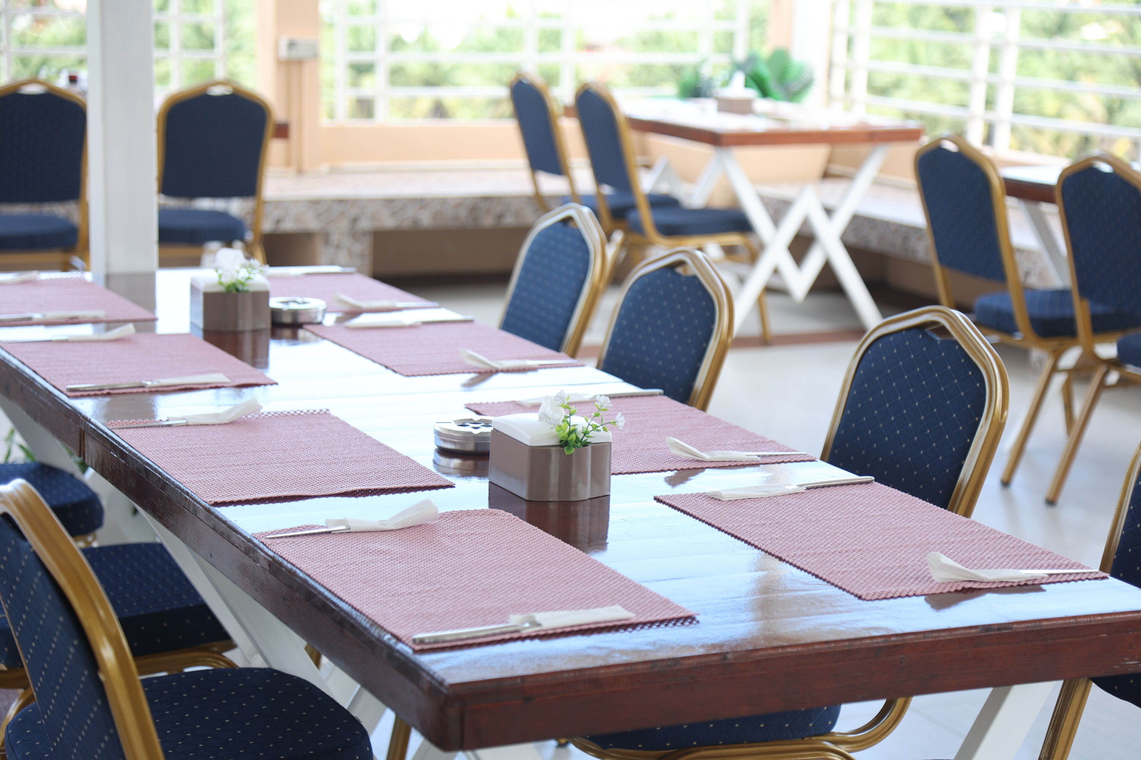 Une salle de conférence dotée d’une longue table préparée pour les réunions, entourée de chaises au revêtement bleu et aux montures dorées.