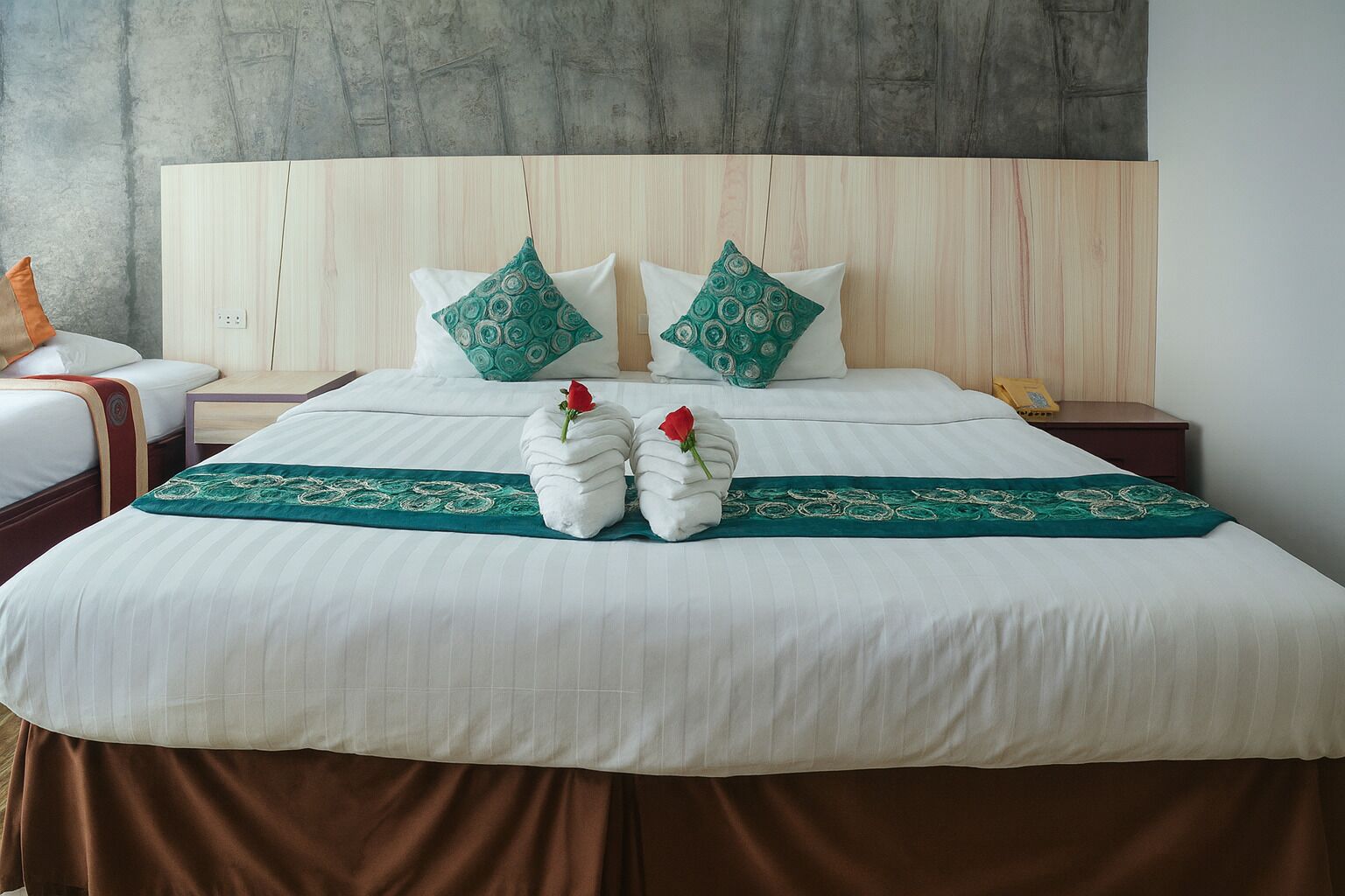 Una cama bien tendida con sábanas blancas, dos almohadas estampadas en verde y un corredor decorativo verde.