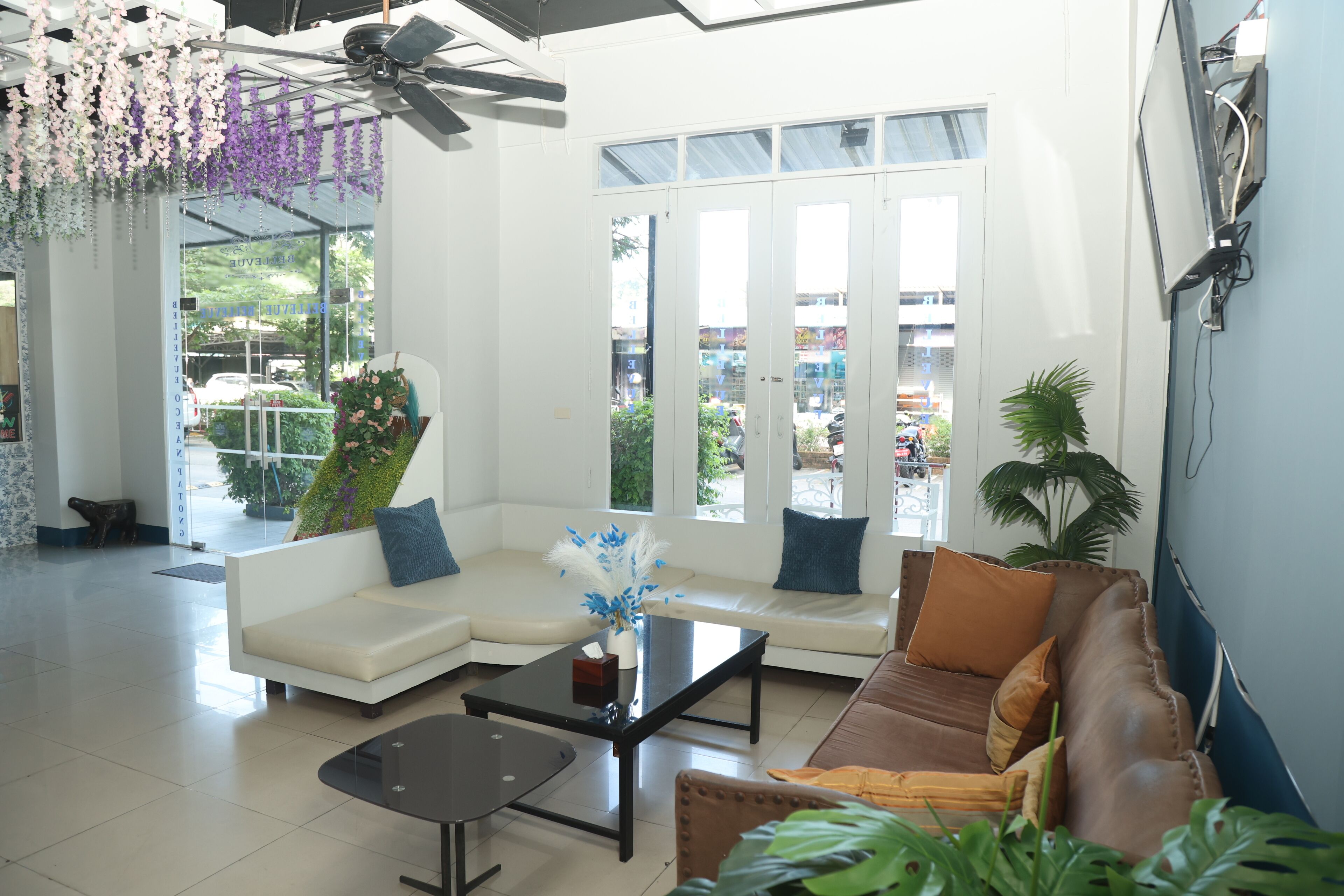 A modern lobby with a white sofa, a brown sofa, a glass coffee table, and a ceiling fan.