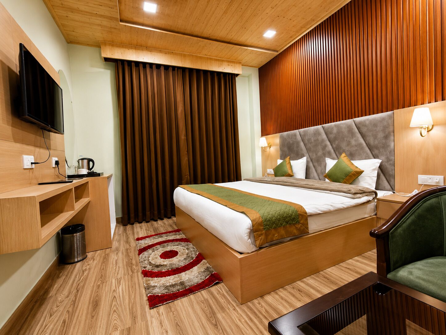 Een hotelkamer met een houten plafond, een bed met hoofdeinde, een aan de muur bevestigde televisie, een nachtkastje en een groene stoel.