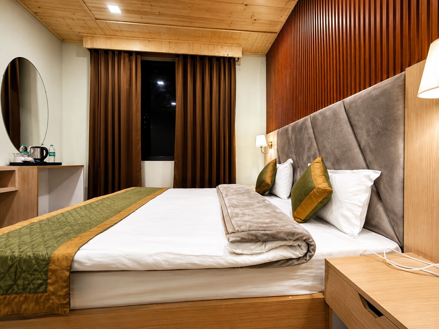 A hotel room with a large bed, a bedside table, a mirror, a window with curtains, and a wooden ceiling.