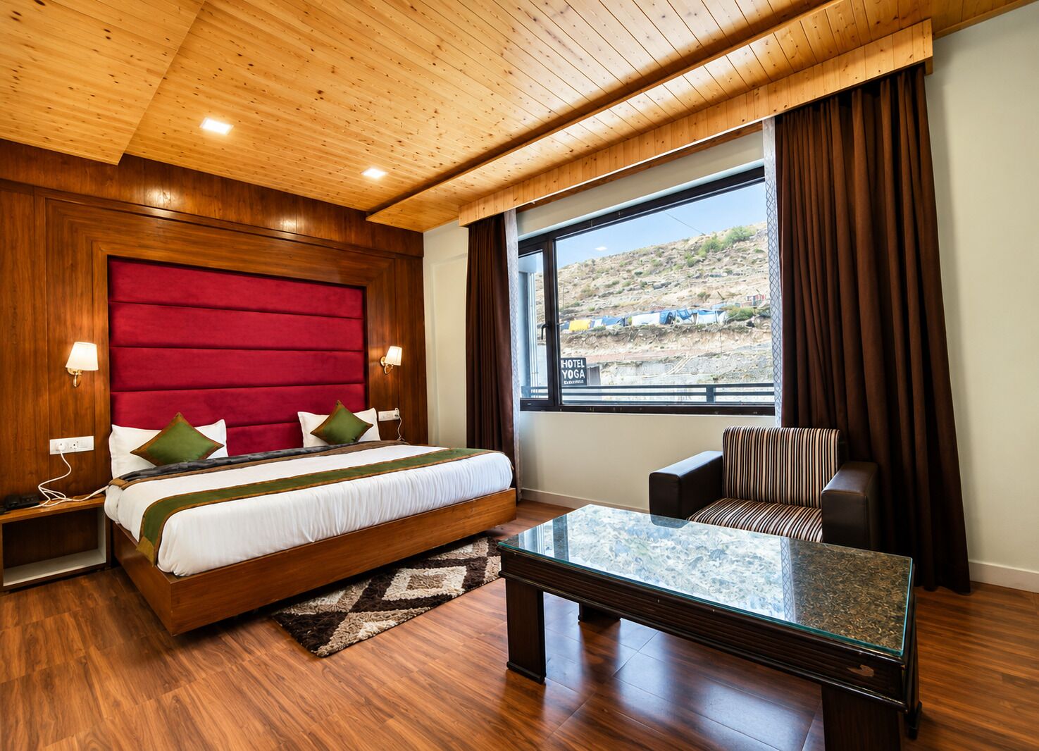 Une chambre d’hôtel avec un grand lit, une table basse en verre, un fauteuil à rayures et une vue sur un paysage désertique.