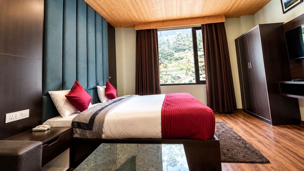A modern bedroom with a wooden ceiling, a large bed with red and white bedding, a TV, and a wardrobe. - ECKO Premier New Yoga (Joshimath)