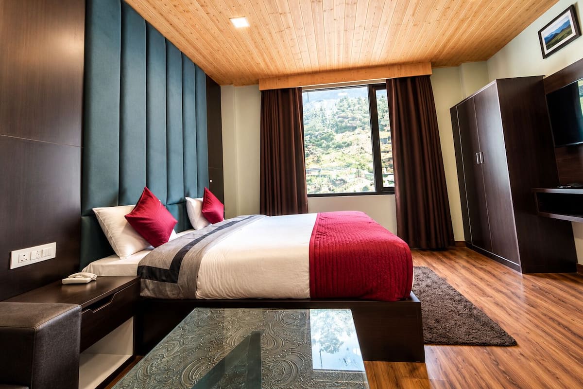 A modern bedroom with a wooden ceiling, a large bed with red and white bedding, a TV, and a wardrobe.