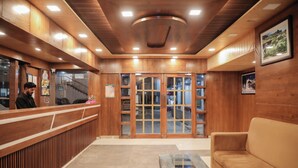 A reception area with a wooden reception desk, a glass coffee table, and a sofa. - ECKO Premier New Yoga (Joshimath)