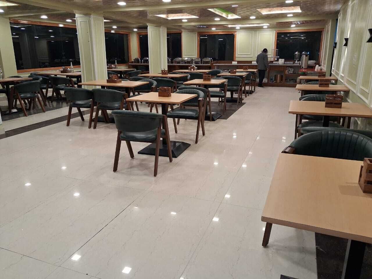 A spacious dining area with multiple tables and chairs, a kitchen area in the background, and a polished tile floor.