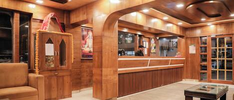 A reception area with wooden paneling, a reception desk, a seating area with a sofa, and a glass-top table.