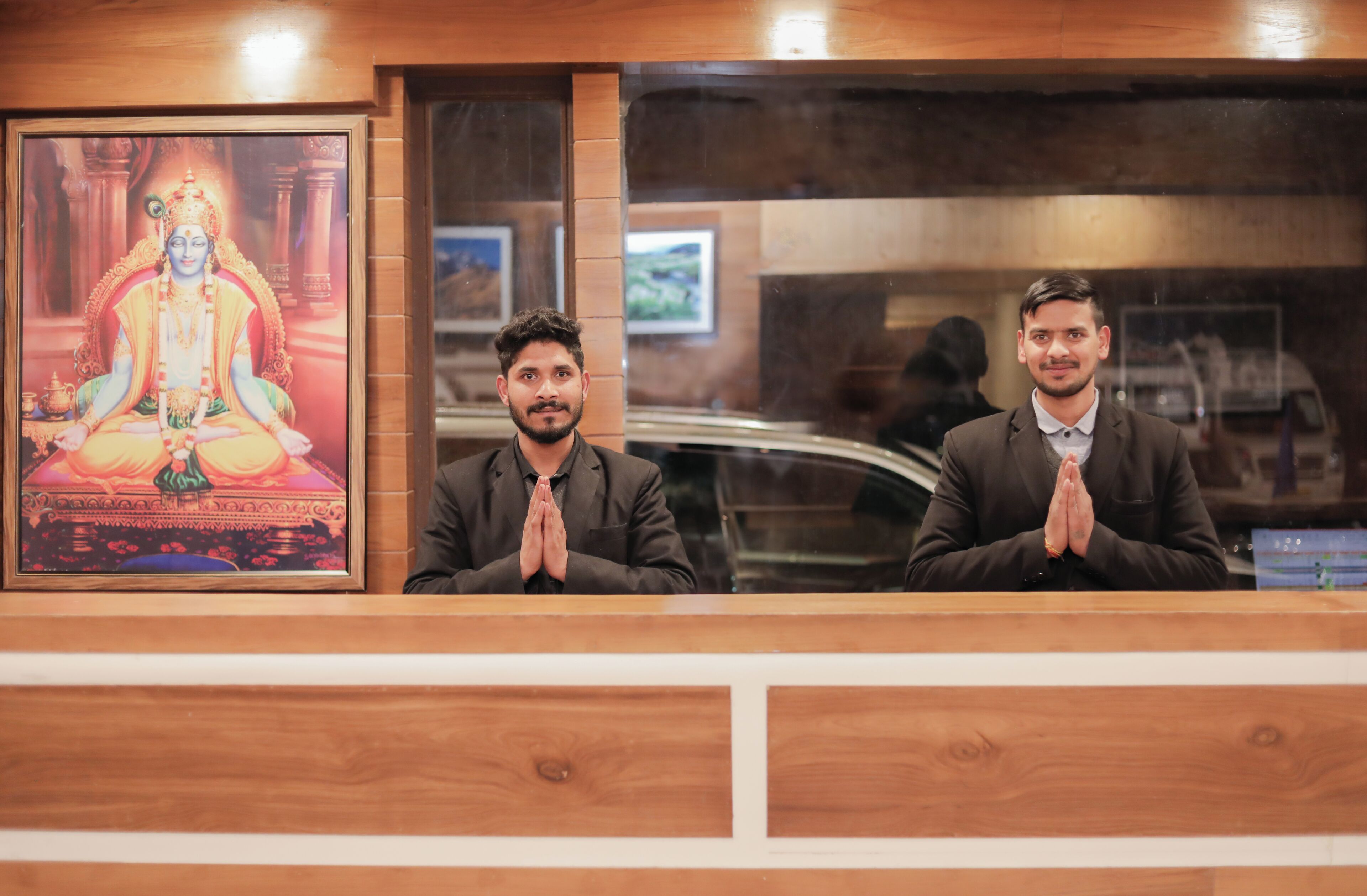 Two men seated at a reception desk with a framed religious painting above them.