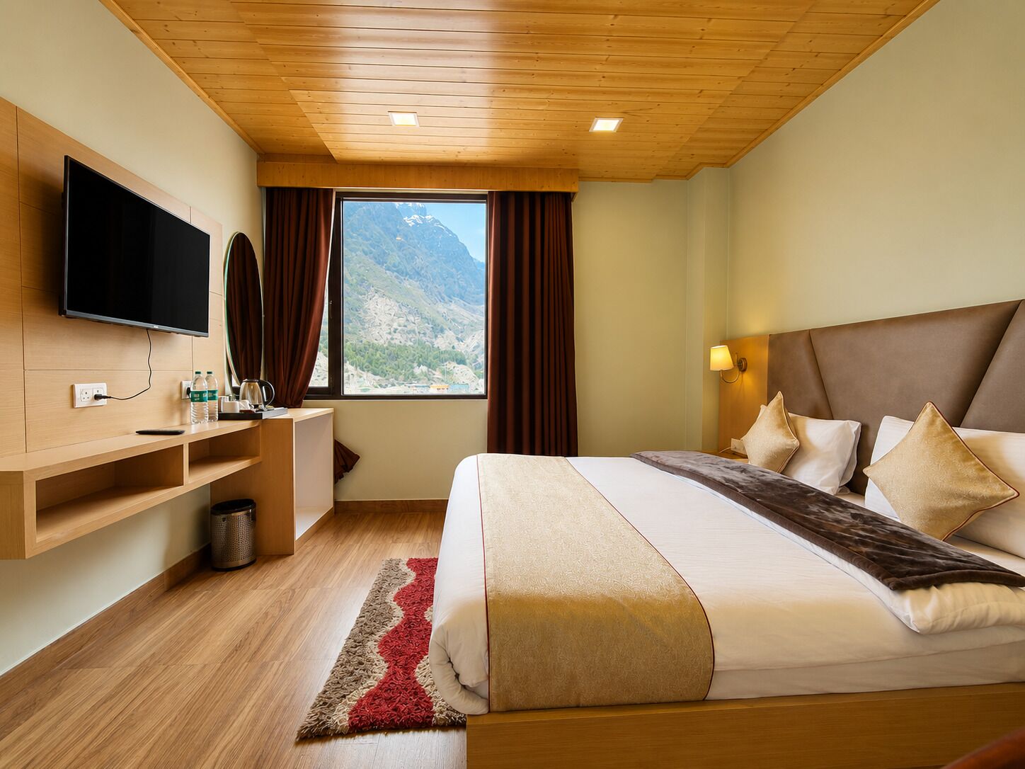 A hotel room with a bed, TV, desk, and a window with a mountain view.