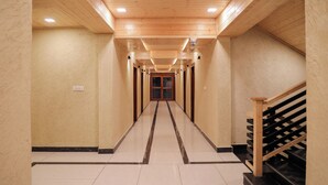 A long, narrow hallway with wooden walls and a tiled floor, leading to a staircase with a wooden railing. - ECKO Premier New Yoga (Joshimath)