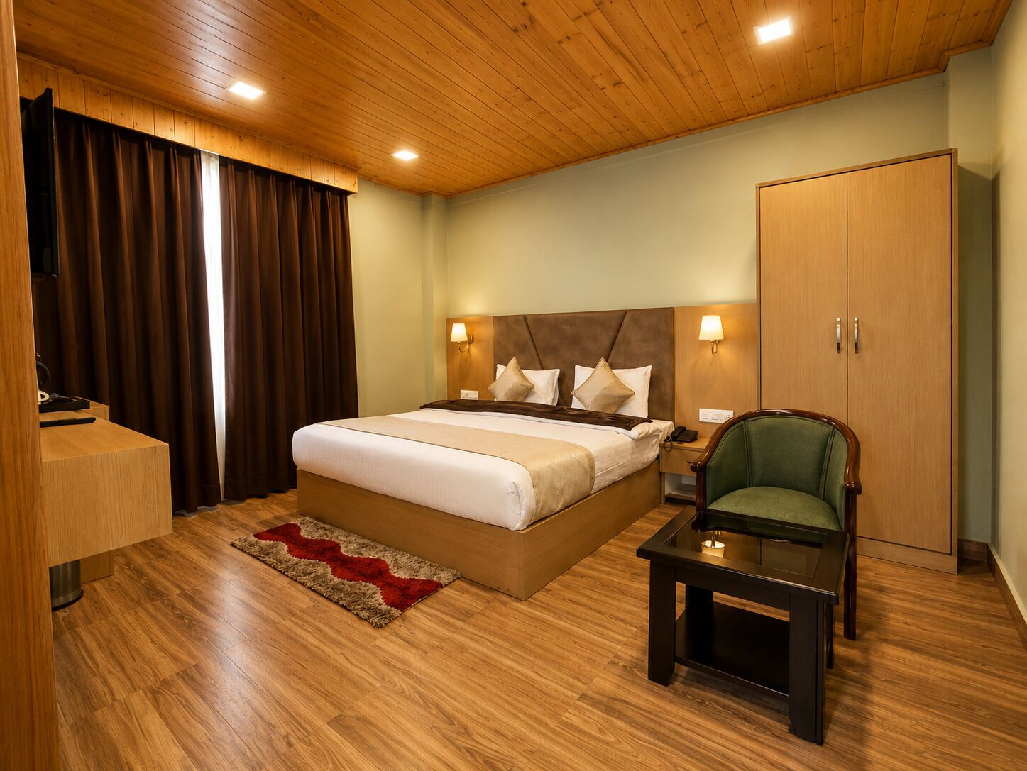 Ein Hotelzimmer mit Holzboden, einem großen Bett mit Kopfteil, einem Nachttisch, einem grünen Sessel, einem kleinen Tisch und einem Kleiderschrank.