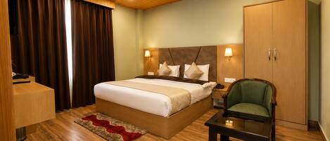 Ein Hotelzimmer mit Holzboden, einem großen Bett mit Kopfteil, einem Nachttisch, einem grünen Sessel, einem kleinen Tisch und einem Kleiderschrank.