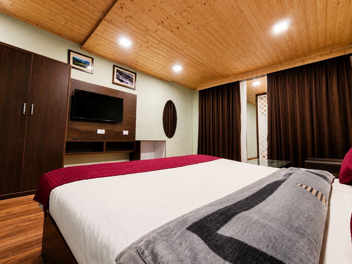 A bedroom with a large bed, wooden wardrobe, a flat-screen TV, and a mirror.