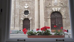 Une façade d’immeuble avec deux grandes portes, une statue au-dessus de la porte de gauche et un parterre de fleurs au premier plan.