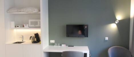 Un espacio habitable compacto con kitchenette, un televisor de pantalla plana en la pared y dos sillas modernas.