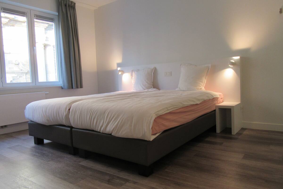 A modern bedroom with a large bed, bedside tables, and a window with curtains.