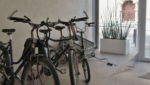 Des vélos sont garés à l’intérieur, avec une plante en pot et l’entrée d’un bâtiment en arrière-plan.