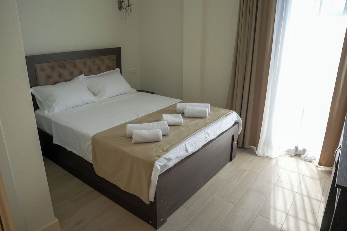 Een netjes opgemaakt bed met witte lakens en een beige sprei, een houten hoofdbord en een bedlampje.