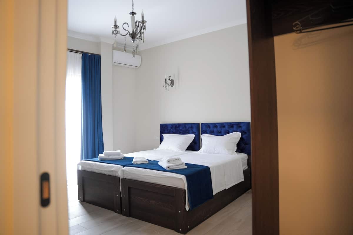 Een tweepersoonsbed met een blauw hoofdeinde, twee nachtkastjes en een kroonluchter.