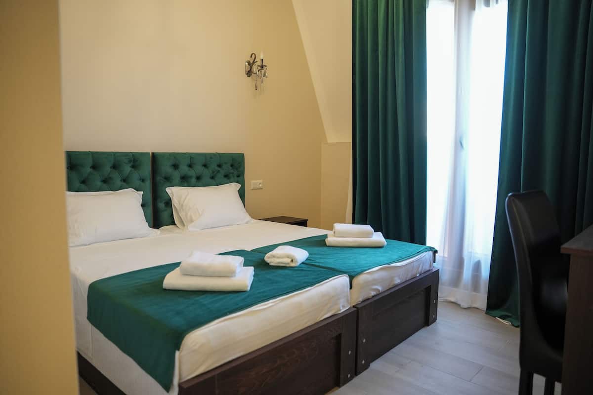 Een tweepersoonsbed met een groen hoofdeinde, wit beddengoed en twee net gevouwen handdoeken.