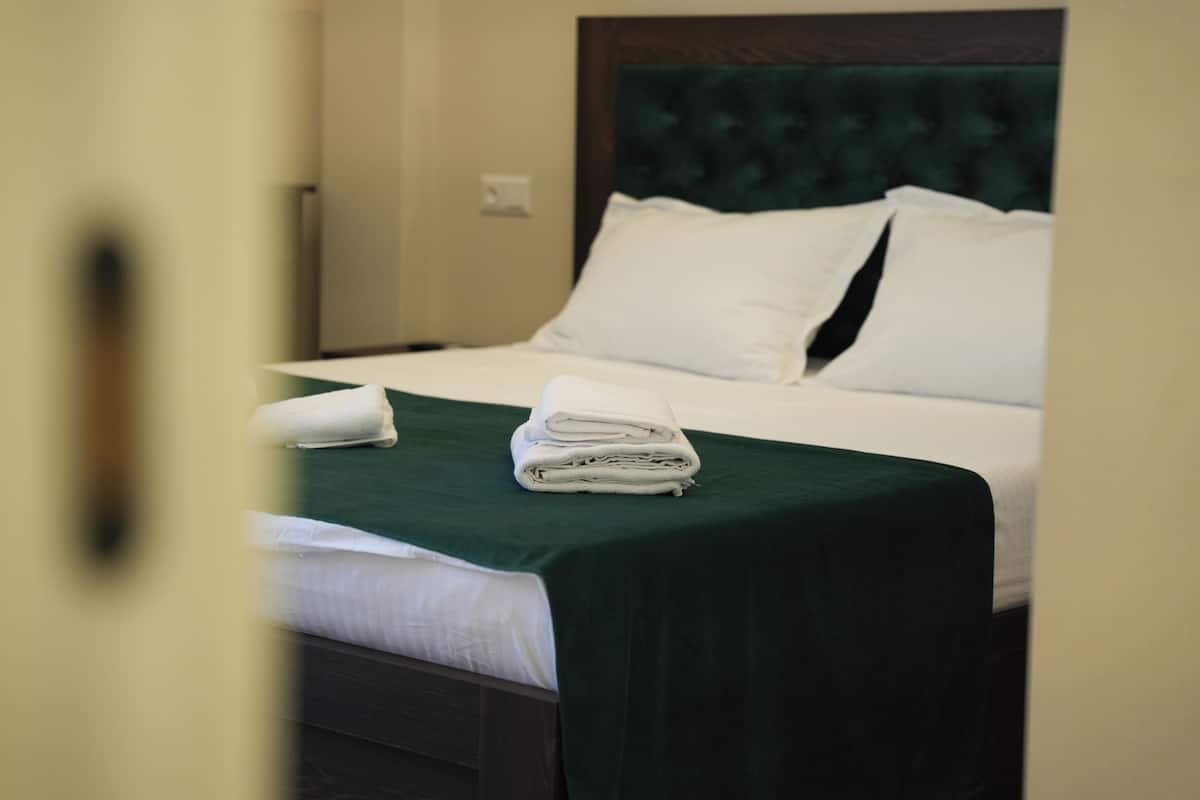 Een net opgemaakt bed met witte lakens, een groene sprei, een houten hoofdbord en een wit kussen.