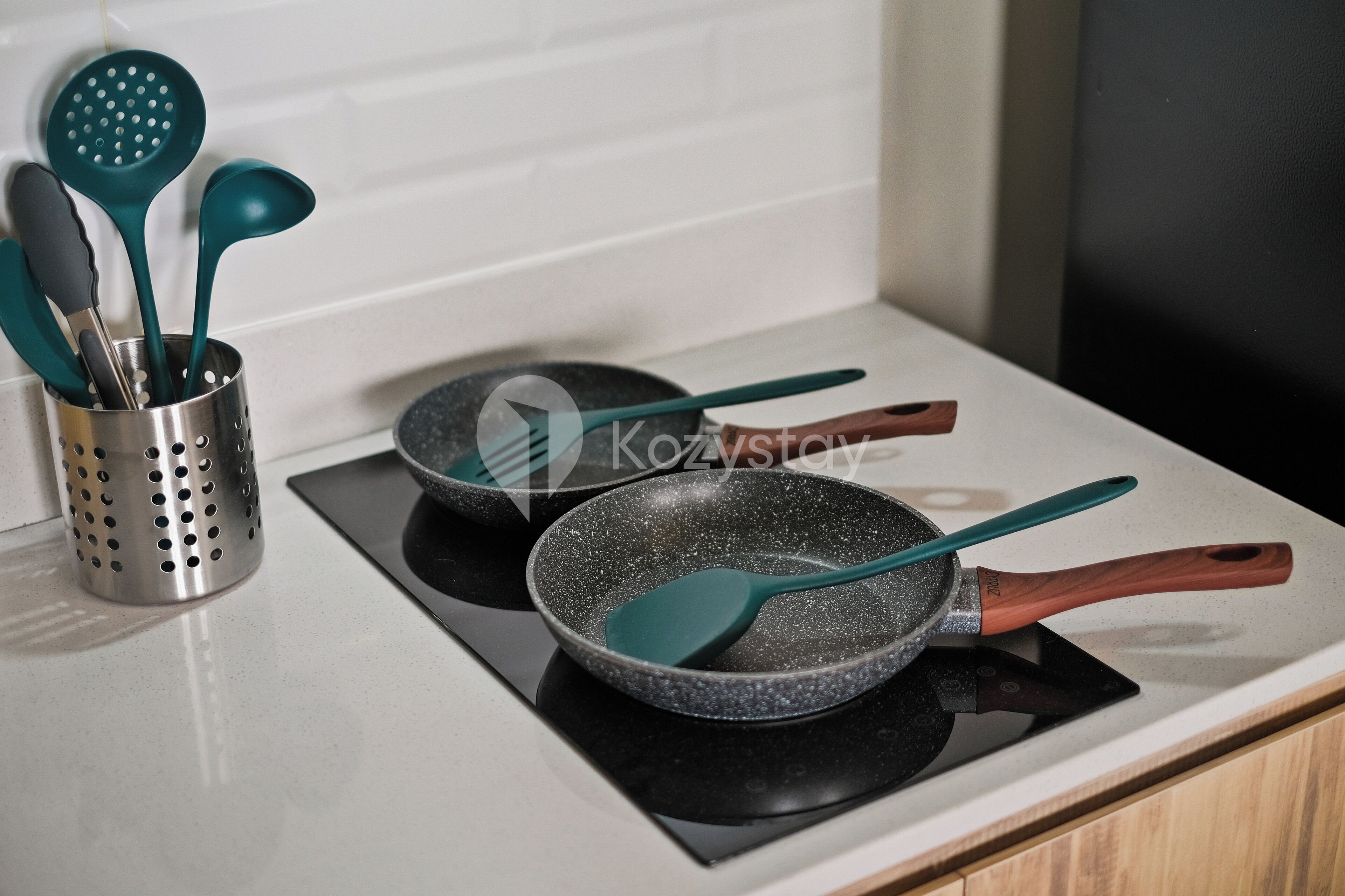 Una cocina con estufa, dos sartenes y un portalápices con diversos utensilios de cocina.
