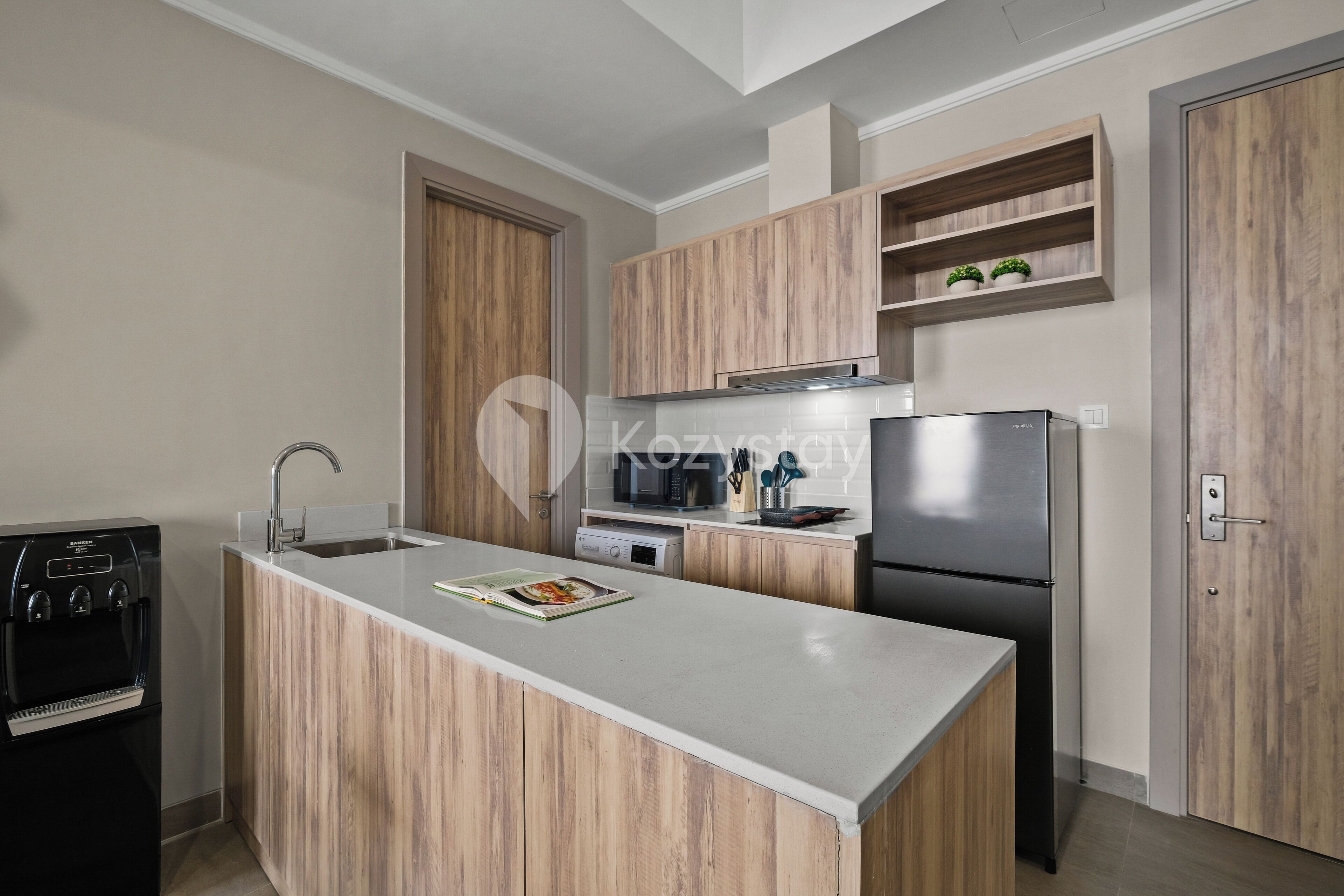 Une cuisine moderne avec des meubles en bois, un four à micro-ondes encastré, un réfrigérateur en acier inoxydable et un distributeur d’eau.
