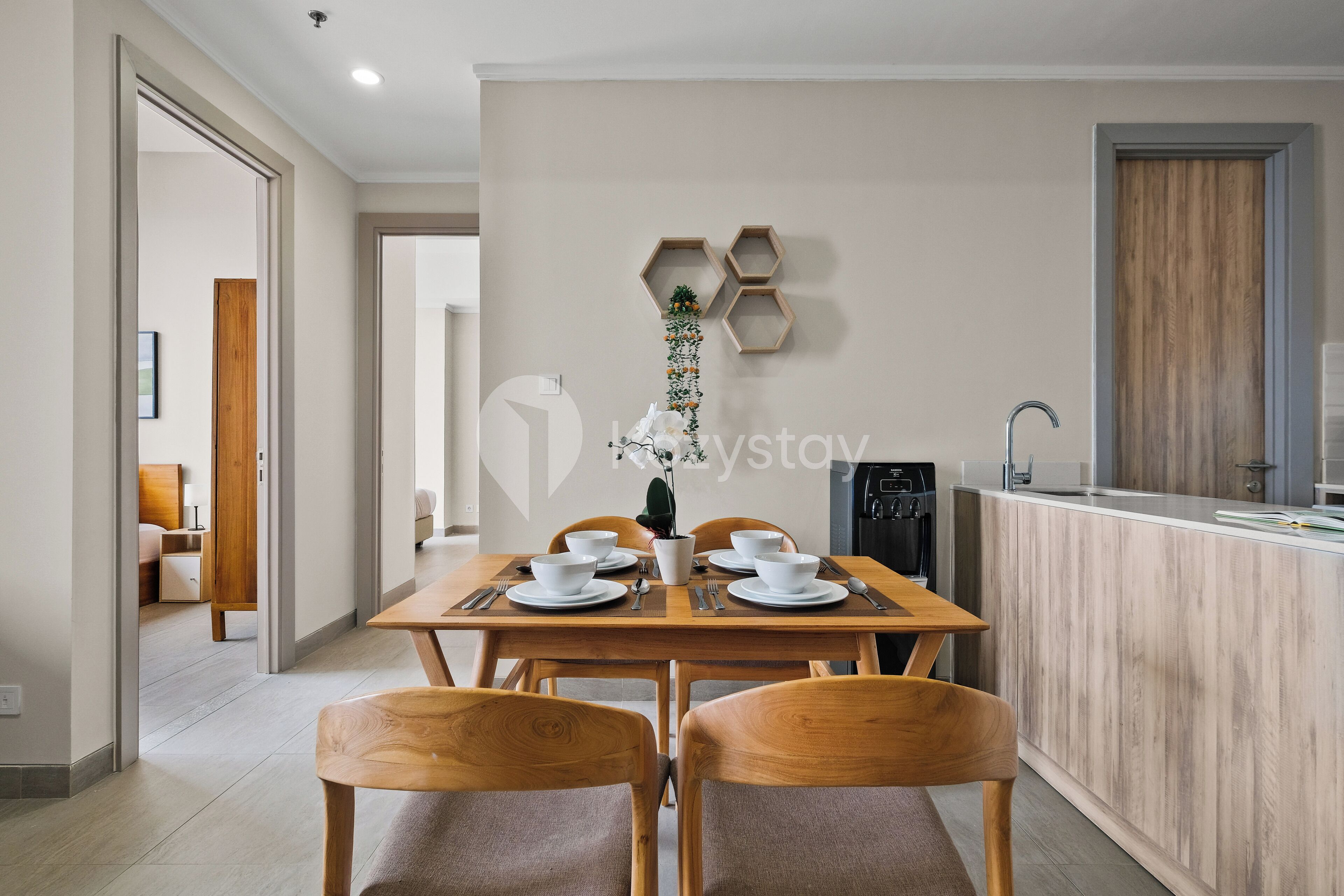 A modern dining area with a wooden table set for four, a kitchen with a built-in island, and a hallway leading to another room.
