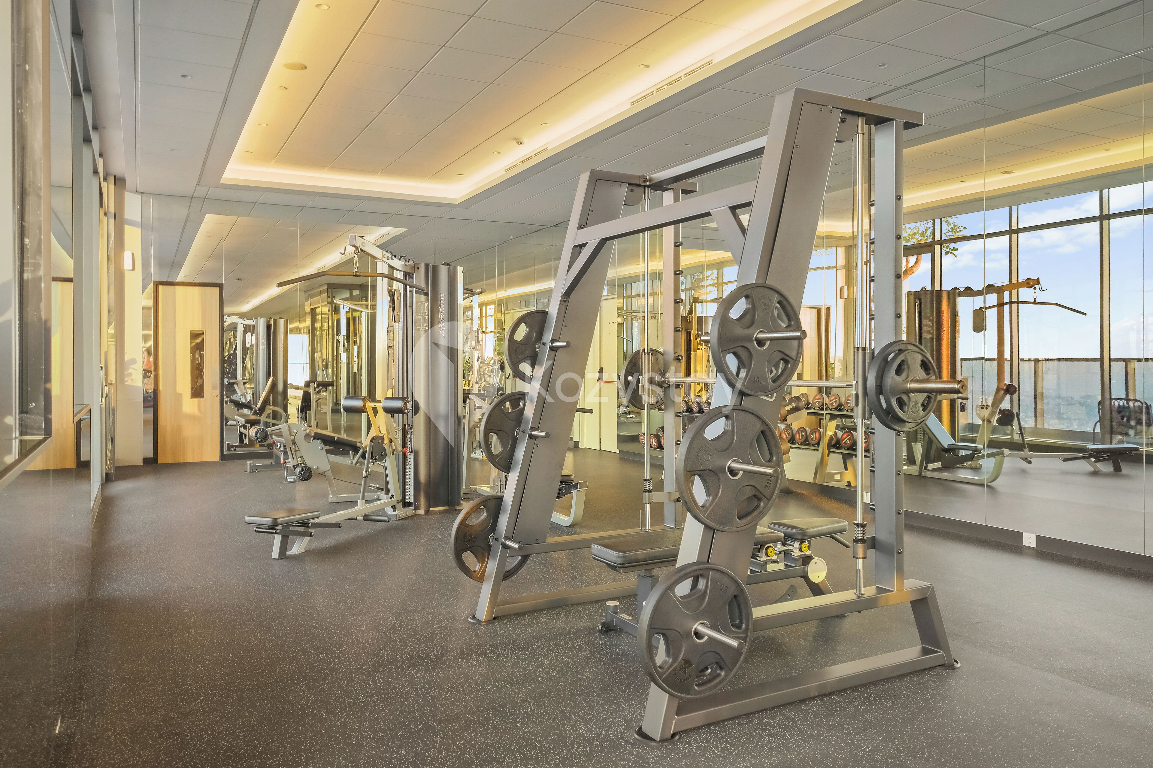 A gym with weightlifting equipment, mirrors, and large windows.
