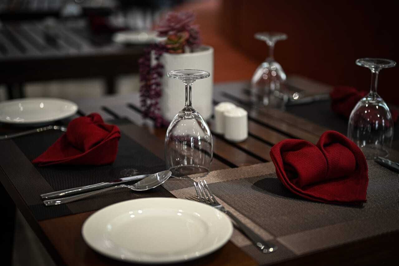 A dining table set with white plates, cutlery, and red napkins.