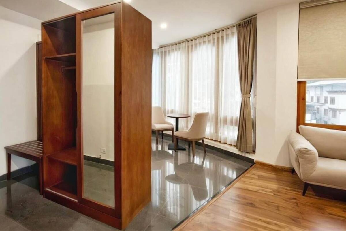 A modern living room with a wooden wardrobe, a sofa, a dining table with chairs, and a large window with curtains.