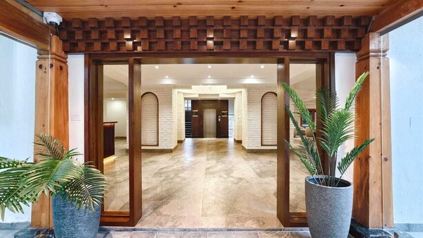 Een hotelingang met een houten plafond, stenen vloer en grote potplanten.