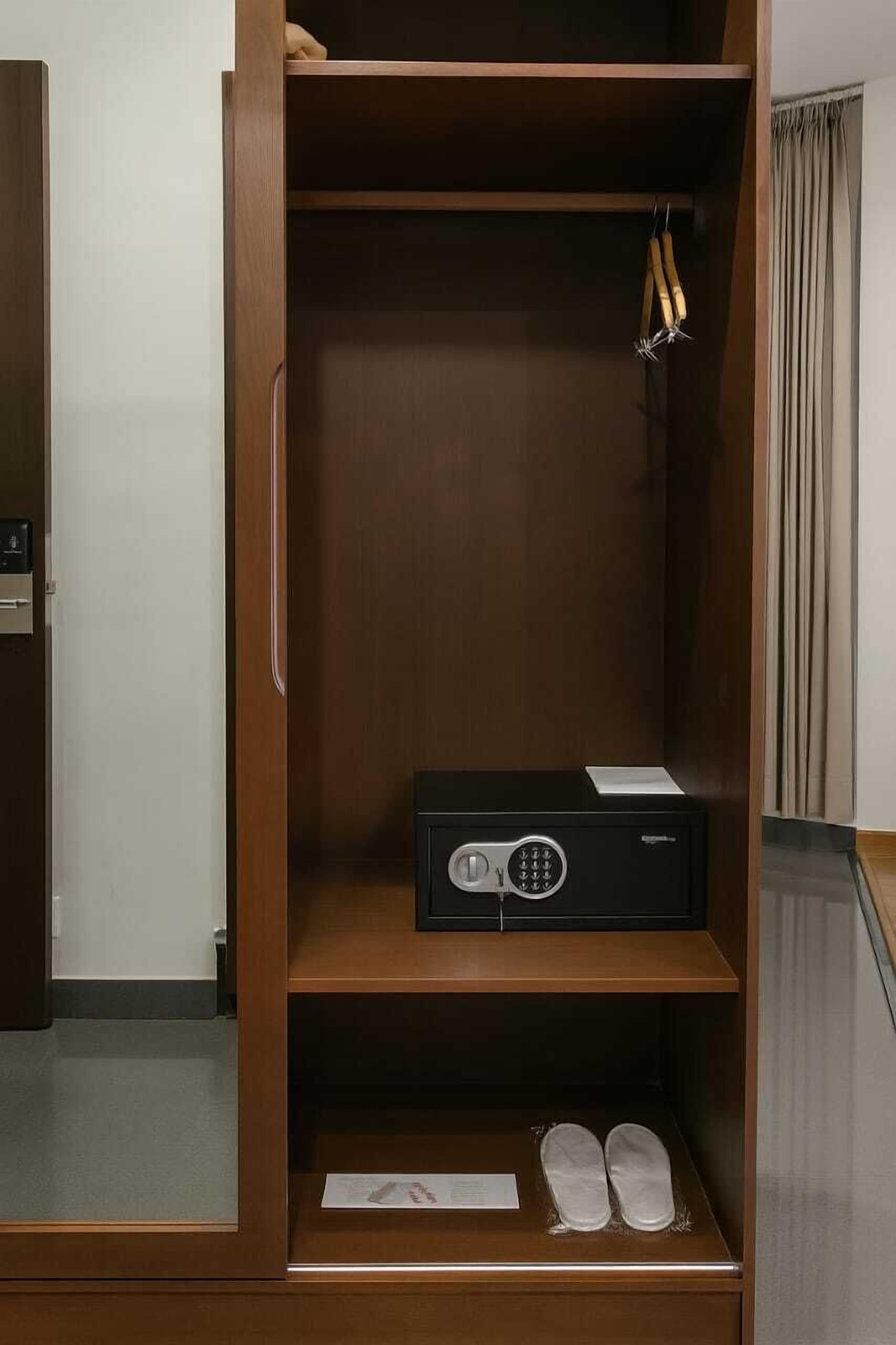 A wooden wardrobe with a safe, a pair of shoes, and a hanging rack.