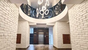 Een ruime, moderne lobby met witte bakstenen muren, een centrale lift en een decoratieve plafondlamp.