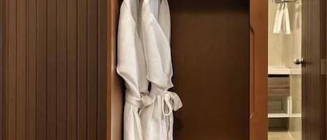 A wooden wardrobe with a hanging robe and a bench.