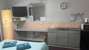 Una habitación de hotel pequeña con una cama, televisor, lavamanos y microondas.