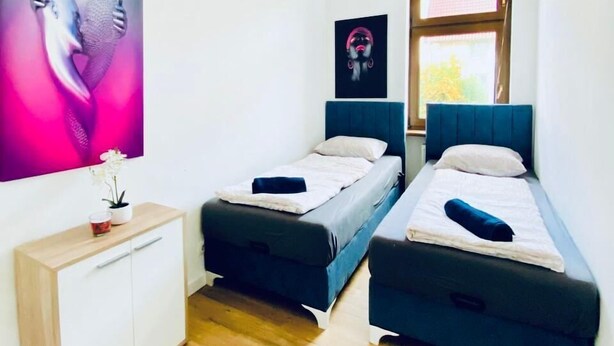 Een moderne slaapkamer met twee eenpersoonsbedden, een houten dressoir en een groot abstract schilderij aan de muur.